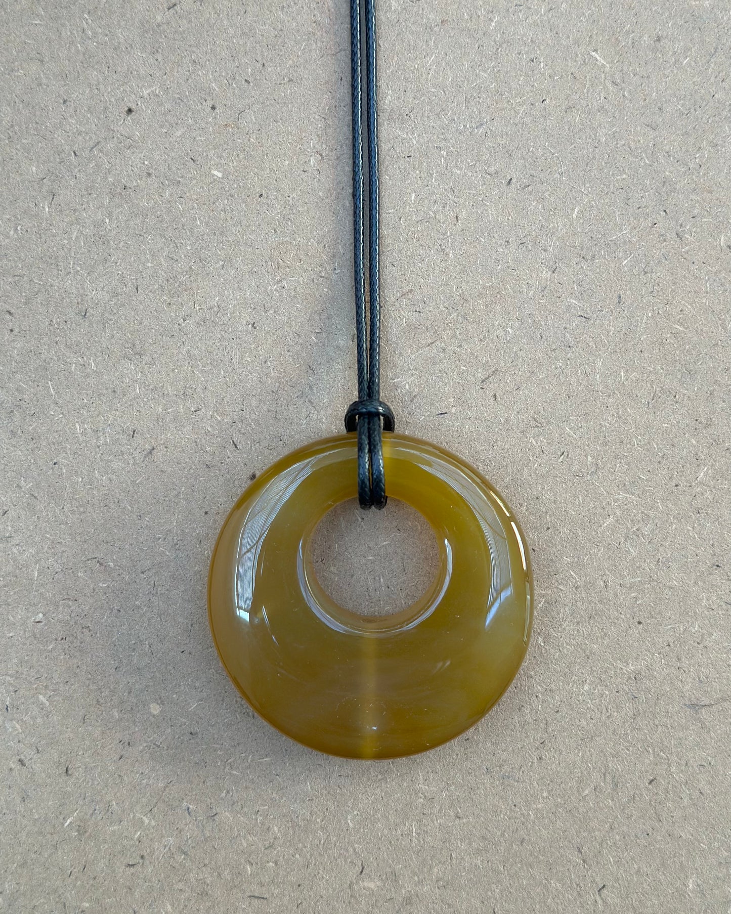 An amber agate hoop necklace with a wax coated polyester cord and a lobster claw closure, displayed against a beige background.
